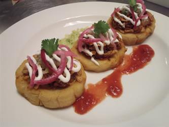Biscuits topped with pork, sour cream, and red onions with a side of red salsa and green salsa.