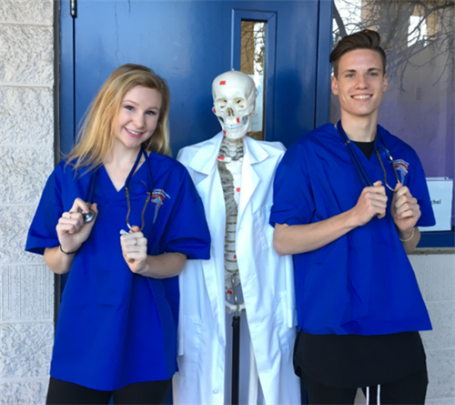 2 students standing in front of a skeleton dressed in a lab coat